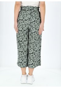 Pantaloni culotte floreali in nero e verde chiaro, con vita elasticizzata e gambe larghe, abbinati a sneaker bianche.
