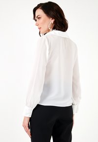 White chiffon blouse with a classic collar, cuffed long sleeves, and a lightweight, semi-sheer texture. Simple design, no patterns.