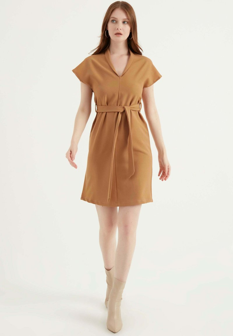 Braunes kurzärmliges Kleid mit V-Ausschnitt, tailliertem Bund und glattem Stoff. Der Saum endet oberhalb des Knies und zeichnet sich durch ein einfaches, strukturiertes Design aus.