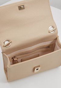 Beige compacte tas met een textuurrijke buitenkant, gouden hardware accenten, een ritsvak en meerdere kaartsleuven aan de binnenkant.