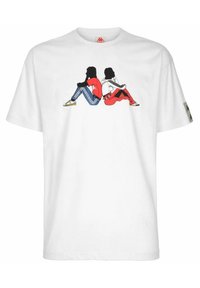 Camiseta blanca con un gráfico de dos figuras sentadas. Una lleva un conjunto rojo y azul, la otra en monocromo, contra un fondo simple.