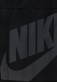 Black fabric featuring a large, matte black Nike logo with a stylized swoosh. The material is textured, adding depth to the design.