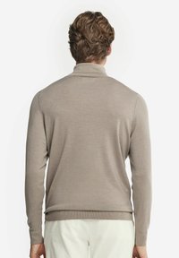 Beige tröja med lång ärm och hög krage, med en slät textur och en figursydd design, sedd bakifrån.