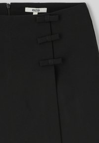 Jupe noire en tissu lisse avec une fente avant, ornée de trois petits nœuds et d'une fermeture à glissière sur le côté.