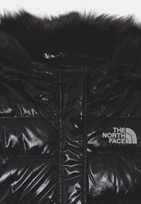 Black puffer jacket with a shiny finish, featuring a fur hood, quilted design, and a white logo on the chest.