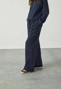 Pantaloni de lounge confortabili, de culoare bleumarin, confecționați dintr-un material moale, cu o croială relaxată și buzunare laterale, asortați cu încălțăminte maro și bej deschis.
