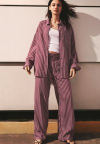 Cămașă supradimensionată cu dungi, de culoare mov deschis, și pantaloni largi asortați, dintr-un material moale și texturat. Maiou alb dedesubt.