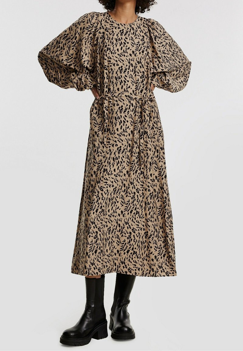 Vestido marrón con estampado abstracto negro, mangas globo y cintura ceñida con cinturón. Combinado con botas negras de tobillo gruesas. Diseño largo y fluido.