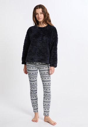Maglietta a maniche lunghe in pile di colore blu scuro con motivo testurizzato, abbinata a leggings bianchi con stampa geometrica blu scuro. La vestibilità delle gambe è aderente.