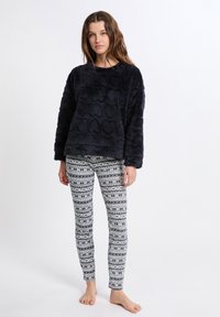 Fleece långärmad topp i marinblått med texturerat mönster, kombinerad med leggings i vitt och marinblå geometriskt mönster. Benen sitter åtsittande.
