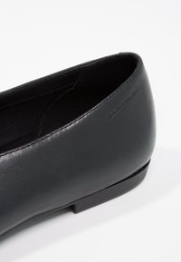 Svart lädersko i platt modell med rund tå, slät yta, minimalistisk design och en låg, solid svart sula. Subtilt präglad logotypdetalj.