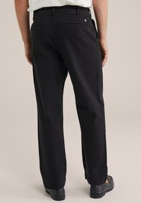 Pantalones de algodón negros con un diseño de pierna recta, dos bolsillos traseros y un detalle sutil en la cintura, combinados con calzado negro.