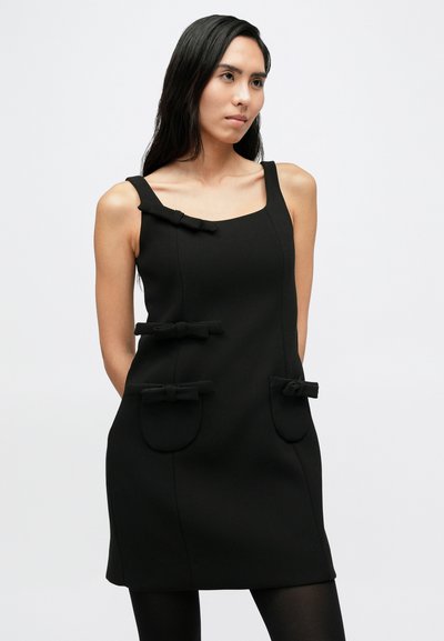 Fekete, ujjatlan ruha négyzet alakú nyakkivágással, négy masni díszítéssel a zsebeknél és az elején. Sima textúrájú, testhezálló szabás.