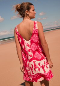 Robe rose sans manches avec un dos plongeant en V, ornée d'un motif coquillages et homards. Confectionnée dans un tissu léger, idéale pour la plage.