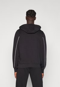 Black hooded sweatshirt made of smooth material with white side stripes, ribbed cuffs, and a relaxed fit design.