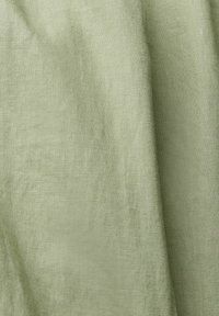 Tela de lino verde claro que muestra una textura tejida visible y suaves pliegues con sombras de luz natural.