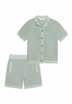 Lysegrøn strikket kortærmet skjorte med krave og matchende strikkede shorts med lommer, lagt fladt på en hvid baggrund.