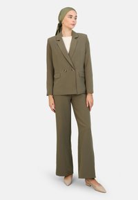Pantalon de costume vert olive avec un blazer croisé et un pantalon large, doté de boutons dorés. Tissu lisse sans motifs visibles.