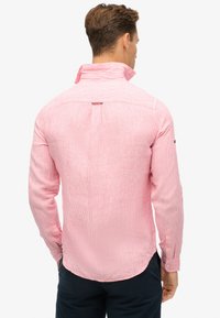 Camisa de manga larga a rayas rosas con cuello, que presenta un detalle en la parte posterior y puños abotonados, hecha de tejido ligero.