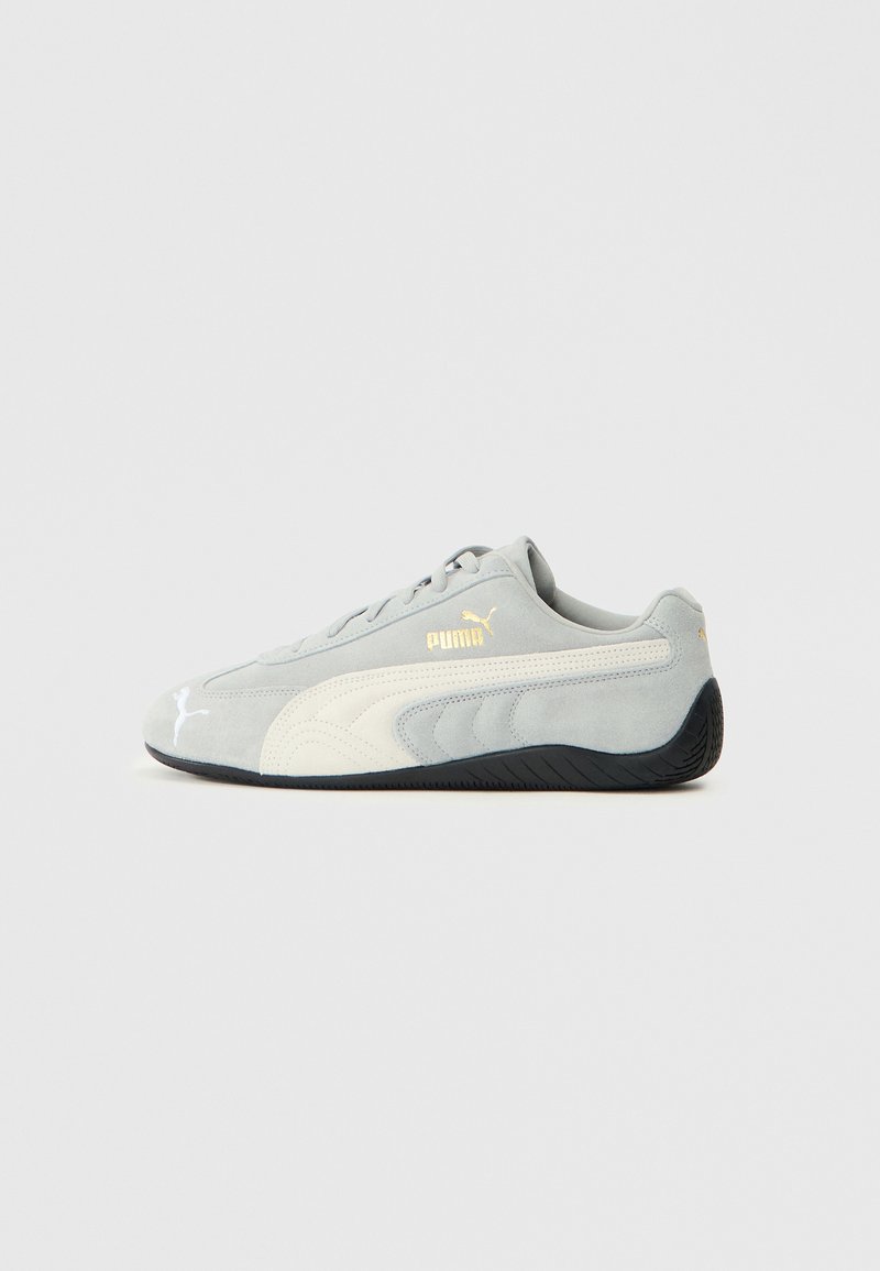 Baskets en daim gris avec des accents blancs et une semelle en caoutchouc noire. Présente un logo doré sur le côté et un design épuré pour le confort.