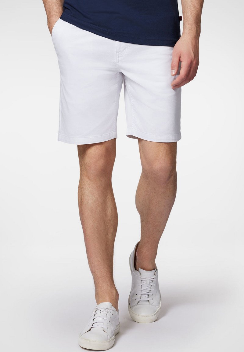 Białe bawełniane szorty o prostym kroju, z gładkim przodem, bocznymi kieszeniami i podwiniętymi mankietami, w połączeniu z białymi trampkami.