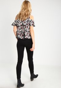 Blouse florale à épaules dénudées avec volants, motif noir et blanc, portée avec un jean noir ajusté et des bottines, vue de dos.