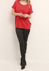 Top rosso a maniche corte con scollatura tonda, abbinato a pantaloni neri aderenti e stivali neri con tacco al ginocchio. Tessuto dalla texture liscia.