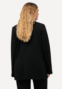 Blazer negro con un corte entallado, abertura simple y puños abotonados. Material suave, hombros estructurados y diseño minimalista.