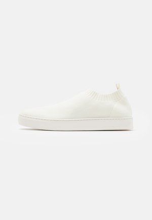 Lavtops hvid strikket slip-on sneaker med ribbet ankelkrave og trækflig på en flad sål, set fra ydersiden.
