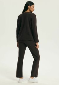 Brązowa bluzka z długim rękawem w zestawie z dopasowanymi spodniami, charakteryzująca się luźnym krojem i gładką teksturą, uzupełniona białymi trampkami.