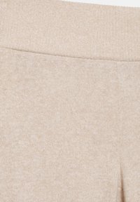 Bézs színű, pamutkeverék anyag lágy tapintással és bordázott derékpánttal. A felület enyhén melírozottnak tűnik egyenletes mintázattal.