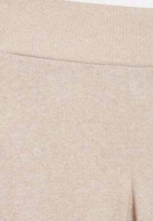 Prim-plan cu pantaloni bej tricotati, prevăzuți cu talie elastică zimțată și material texturat moale.