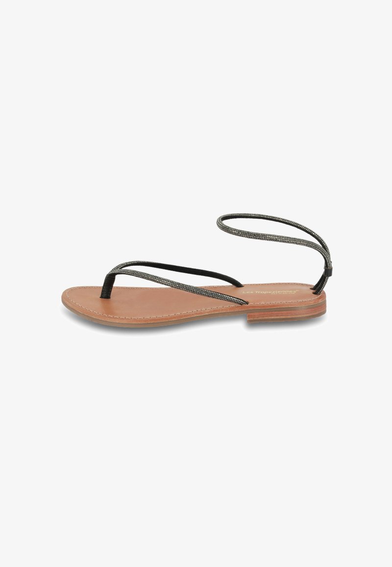 Sandales plates avec une semelle en cuir marron, présentant de fines lanières noires et un design unique de bride de cheville. Style minimaliste et ouvert sur l'avant.