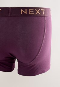 Boxer da uomo viola con fascia elastica larga e marchio dorato "NEXT" su sfondo neutro.