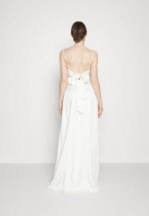 Witte satijnen jurk met een lage rug, dunne bandjes en een strikdetail op de taille. De rok stroomt elegant naar de vloer.
