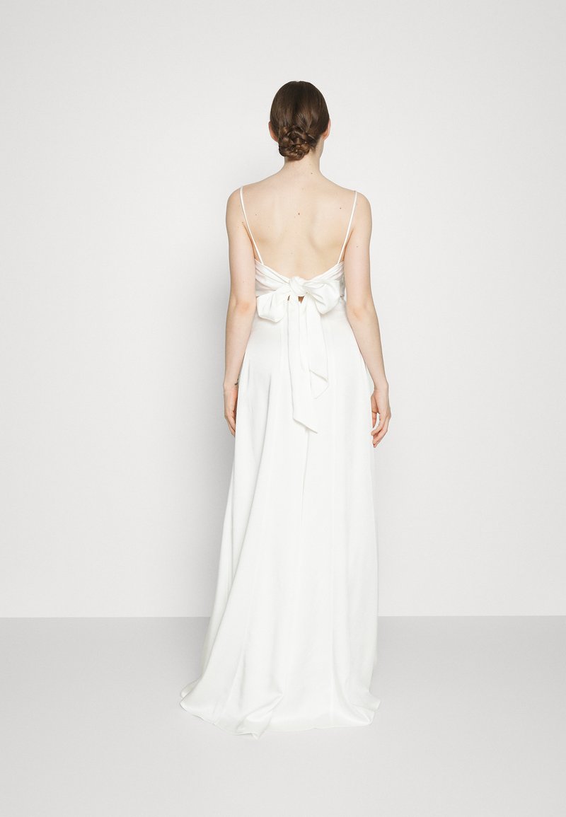 Witte satijnen jurk met een lage rug, dunne bandjes en een strikdetail op de taille. De rok stroomt elegant naar de vloer.