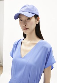 Gorra azul claro con texto bordado y visera curva, combinada con un vestido en v de tela suave, que cuenta con mangas cortas.