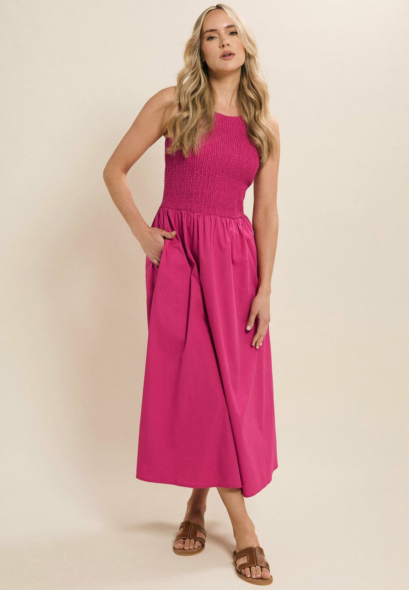 Fuchsia-maxikleid mit gerafftem Oberteil und Seitentaschen; leichter Stoff, A-Linien-Schnitt und ärmelloses Design. Braunfarbene Riemchensandalen getragen.