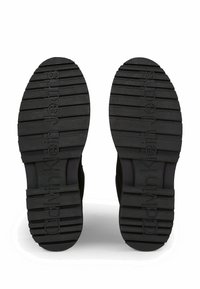 Suole di scarpe in gomma nera con modelli di grip testurizzati e dettagli del logo. Il design presenta scanalature orizzontali e una forma piatta e arrotondata.