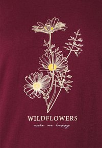 Bordeaux shirt met wit en geel bloemontwerp en de tekst "WILDFLOWERS" en "maak me gelukkig" eronder. Zacht materiaal met gedetailleerde illustratie.