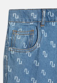 Tessuto denim di colore azzurro chiaro con un motivo a logo bianco ripetuto. Presenta una piccola tasca frontale e cuciture arancioni a contrasto.