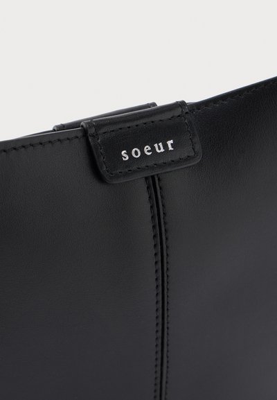 Κοντινό πλάνο μαύρου δερμάτινου μποτάκι με κάθετες ραφές και μια μικρή μαύρη ετικέτα με λευκό κείμενο "soeur".