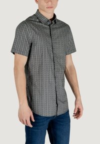 Camicia a maniche corte con bottoni in bianco e nero con un motivo geometrico ripetuto. Realizzata in tessuto leggero con colletto a punta.
