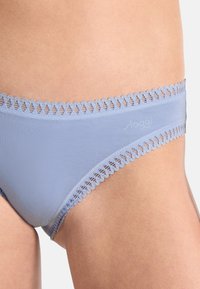 Světle modré spodní prádlo s měkkou, hladkou texturou. Vybaveno ozdobnou krajkovou lemovkou podél pásku, která předvádí jemný vlnkový design.