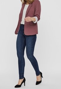 Dopasowane, ciemnoniebieskie dżinsy w parze z różowym żakietem i szarym topem; cechują się gładkimi fakturami i spiczastymi czarnymi szpilkami.