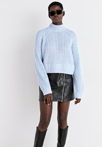 Ανοιχτό μπλε πλεκτό πουλόβερ με ψηλό λαιμό, ριγωτούς καρπούς και χαλαρή εφαρμογή, συνδυασμένο με μια μαύρη δερμάτινη μίνι φούστα και μαύρες μπότες μέχρι το γόνατο.
