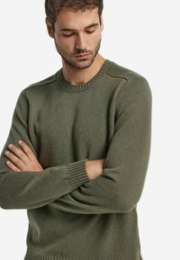 Zielony sweter z dzianiny o okrągłym dekolcie, długich rękawach, ściągaczach i lekko teksturowanym wykończeniem. Prosty, klasyczny design.