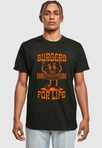 Melnas kokvilnas T-krekls ar oranžu karikatūras burgera grafiku ar rokām, tekstu "BURGERS FOR LIFE" un šaha motīvu zem tā.
