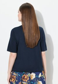 Top de manga corta azul marino hecho de tejido suave, con un ajuste relajado y una textura lisa. Se muestra desde la parte de atrás, combinado con una falda floral.