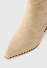 Pointed-toe beige suede ankle boot with a smooth texture and a minimalistic design, featuring a low heel and a clean silhouette.